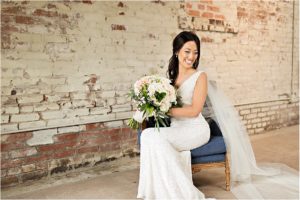 a bride holding her wedding bouquet and sitting on a chair looking away from the camera