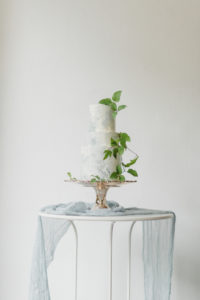 a white wedding cake with blue accents and blue drapery in front of a white wall at a seattle micro wedding venue