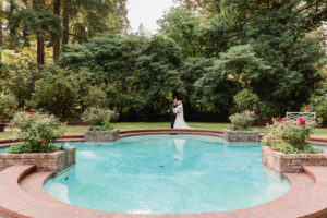a bride and groom standing in front of a large pool in a garden at lakewold gardens wedding venue in seattle