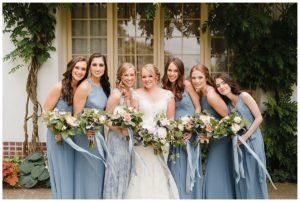 a bride and her bridesmaids in blue dresses all huddled around together holding their whimsical wedding bouquets