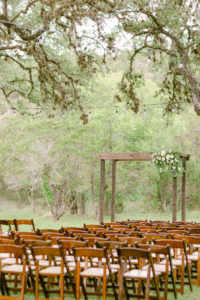 a wedding ceremony design setup with wooden chairs and green trees all around