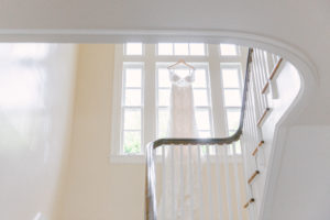 a white wedding dress hanging from the window near white staircases