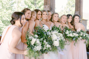 a bride and many bridesmaids huddled together with their bouquets and smiling at swiftwater cellars in washington