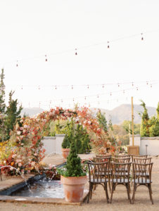 wooden chairs and a fall colored floral arch set up on top of a water fountain for a fall wedding at Hotel Domestique