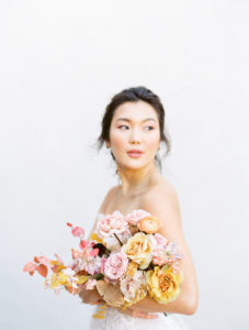 an asian bride holding her bright colored wedding bouquet and looking off into the distance