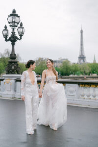 two brides in white dresses walking on the pont alexandre bridge in paris france