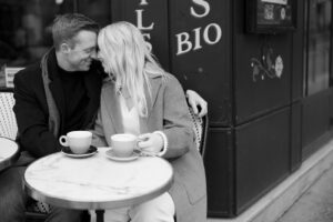 a black and white photo of a man and woman with their foreheads together sitting outside of a cafe in paris 