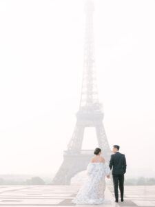 a bride and groom holding hands and walking away from the camera with the eiffel tower in the background