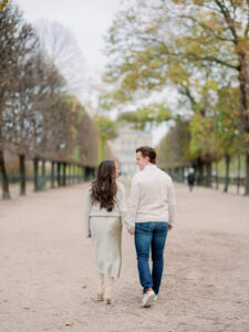 a man and woman walking away from the camera and holding hands in front of the louvre in paris