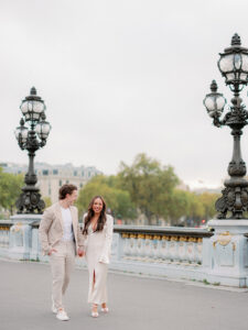a man and woman in white and beige outfits walking towards the camera in Paris for their destination engagement session