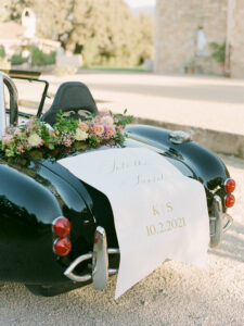 a fancy black car in front of sunstone winery with a sign and flowers on the back