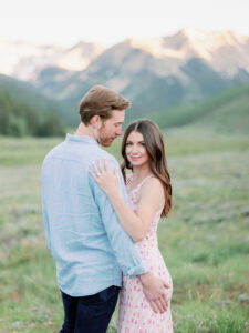 a man in a blue shirt with his back to the camera looking at a woman in a pink dress with the aspen mountains in the background