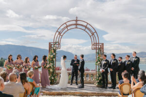 a bride and groom standing at the alter on their wedding day with lake chelan behind them and their bridal party standing besides them