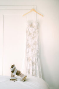 a wedding dress hanging up and wedding shoes sitting on a bed in front of the dress
