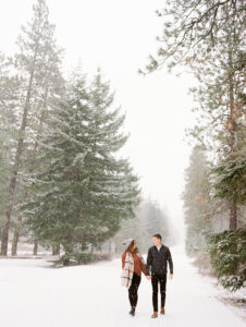 a girl and boy holding hands in the snow walking towards the camera on a snowy road in suncadia washington