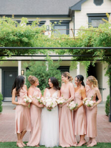 a bunch of bridesmaids huddled together and looking and laughing at each other at a wedding venue in sonoma