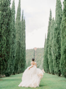a bride running away from the camera in a row of trees at cetinale in italy