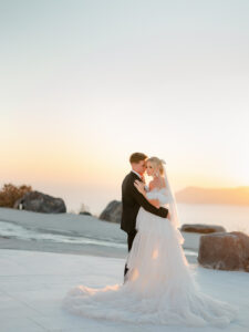 a bride and groom snuggling on the cliffs of santorini greece during sunset for their wedding photos