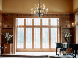 large windows and a grand piano with a beautiful chandelier at the lairmont manor wedding venue in bellingham washington 