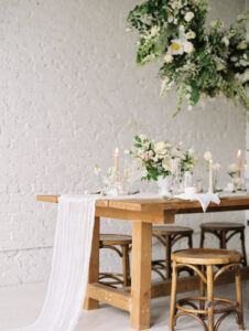 a wooden wedding table set up with white linens and florals in a white studio at the 101 in seattle for a wedding