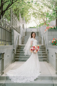 a bride looking down at her colorful bouquet at the draper utah LDS temple with stairs behind her