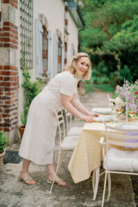 a woman in a dress setting a beautifully decorated table outside a french styled cottage in champagne france