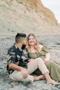 a couple snuggling on the beach at torrey pines and looking happy