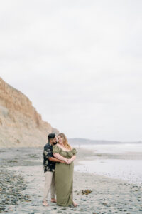 a couple standing on the beach and cuddling together for their torrey pines beach engagement session