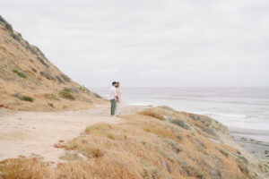 a man and woman holding each other on a cliff at Torrey Pines beach, a great spot for a torrey pines engagement