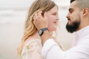 a man playing with a womans hair and looking lovingly into her eyes at their beach engagement session