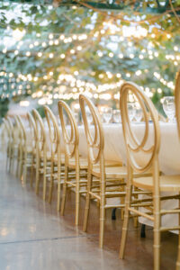 hold chairs in a line with greenery and twinkling lights blurred out above in the background at a utah wedding venues