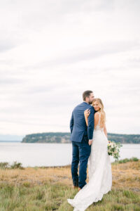 a groom kissing his bride on the forehead overlooking the water at their wedding at chambers bay golf club in tacoma