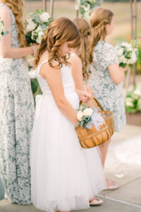 a flower girl with brown curly hair looking down at her basket of flower petals