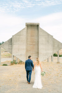 a bride and groom walking towards a large cement sculpture at their wedding venue at chambers bay golf club in tacoma