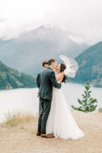a bride and groom kissing with mountains and lakes behind them for their elopement on what is an elopement