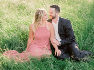 a couple sitting in grass at their discovery park engagement session with a seattle engagement photographer