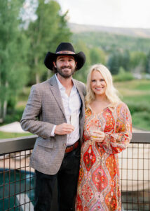 a couple standing and holding drinks while smiling at the camara
