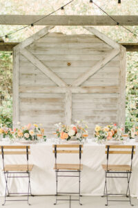 a wedding reception table in front of a white wooden wall with colorful florals and wooden chairs at a wedding venue in snohomish