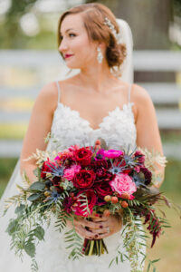 a bride looking away holding her wedding bouquet that is bright pops of pink and reds