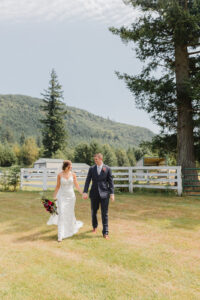 a bride and groom walking towards the camera looking at each other and smiling with a mountain behind them at their fox hollow farm wedding venue