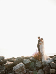 a bride and groom standing on rocks overlooking the ocean in seattle at their edgewater hotel wedding