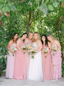 a bride standing in the middle of her bridesmaids wearing pink dresses and holding bouquets while smiling at the camera