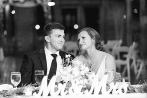 a black and white photo of a bride and groom sitting in front of a sign that says "mr and mrs" and looking at one another