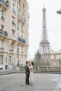 a couple facing each other and embracing on the streets on paris with the eiffel tower behind them for their engagement session in paris