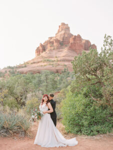 two brides embracing in front of a large red rock formation for their elopement in sedona