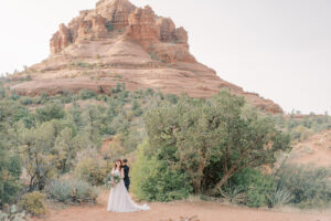 two brides embracing in front of a large red rock formation at their sunrise sedona elopement
