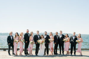 a bridal party in black suits and pink dresses on the dock of the woodmark hotel in kirkland washington for a wedding