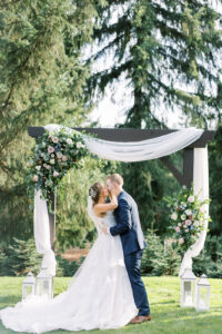 a bride and groom kissing at the wedding alter that is decorated with florals and draped fabric at a wedding at trinity tree farm