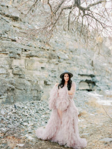a woman in a mauve fluffy dress standing in the snow with rocks behind her for her portaits in provo canyon