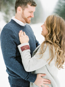 a close up of a couple looking at each other and smiling during their winter engagement photoshoot in the snow